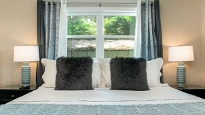 A neatly made bed with two fluffy pillows, a light blue knitted throw, and two bedside lamps on matching nightstands.