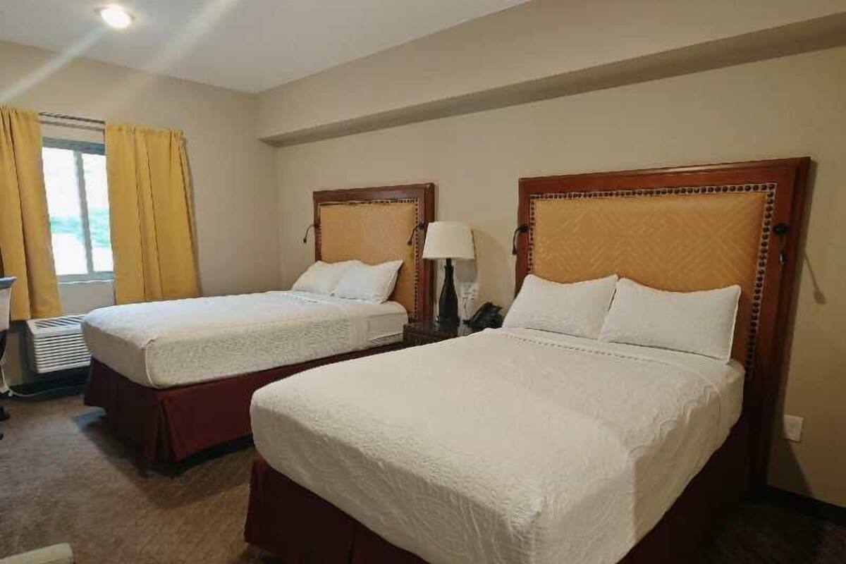A hotel room with two single beds, a desk, and a window with curtains.