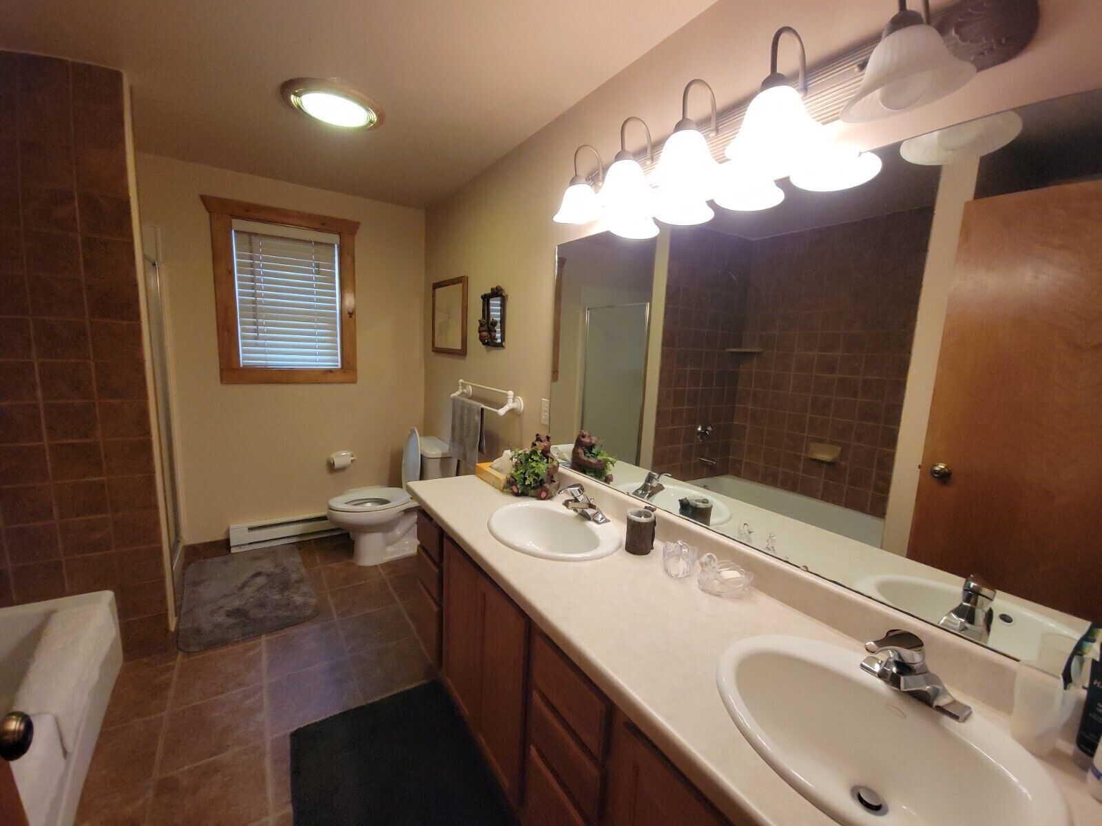 A bathroom with two sinks, a large mirror, and a window with blinds.