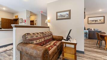 A cozy living area with a brown leather sofa, a small wooden table, and a kitchen in the background.