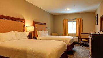 A hotel room with two beds, a desk, a chair, and a window with curtains.