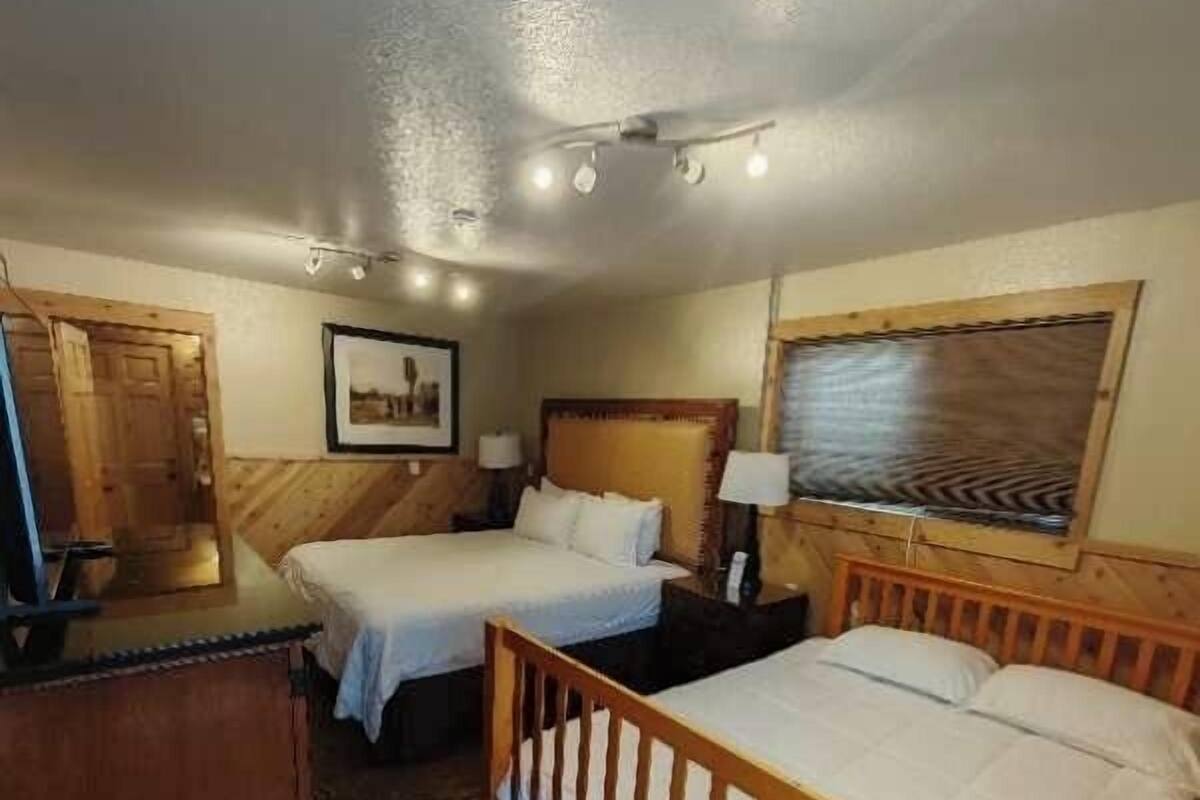 A hotel room with two single beds, a wooden headboard, a desk with a chair, and a large window with a view.