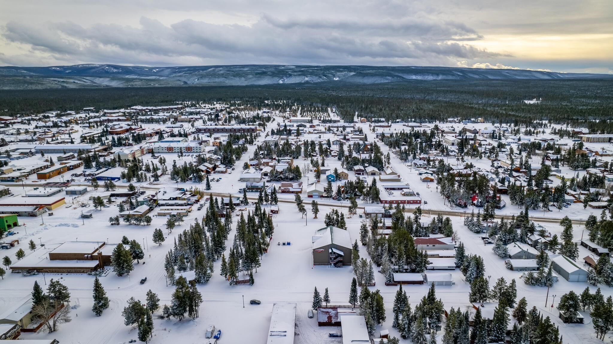 Vue aérienne d’une ville enneigée, avec ses bâtiments et ses arbres, entourée de montagnes.