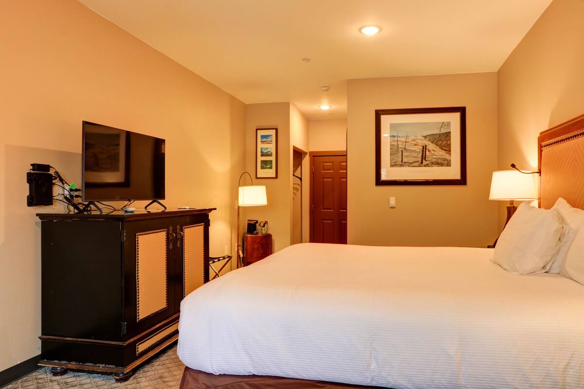 A hotel room with a large bed, a dresser, a television, and a framed picture on the wall.