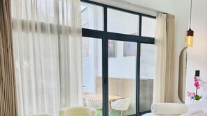 Een moderne slaapkamer met een groot raam, een bed, twee fauteuils en uitzicht op een terras.