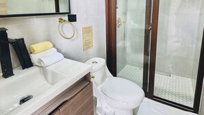 Een badkamer met een wit wastafelmeubel, een toilet en een douchecabine met glazen wanden.
