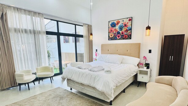 Een moderne slaapkamer met een groot bed, een slaapbank, een nachtkastje en een plafondventilator.