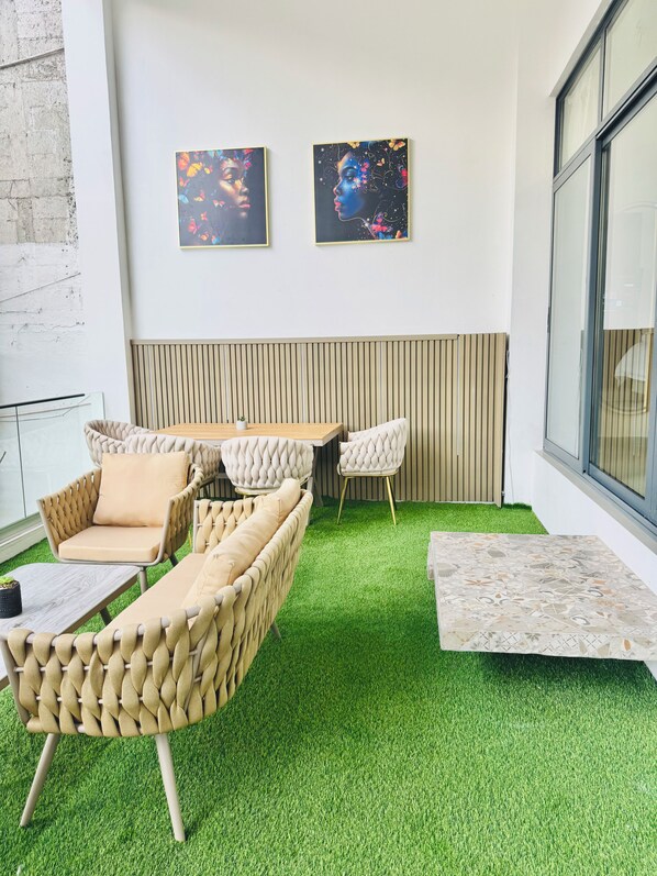 Un moderno espacio lounge con un sofá, sillas y una mesita, con suelo de césped artificial verde y dos cuadros abstractos en la pared.