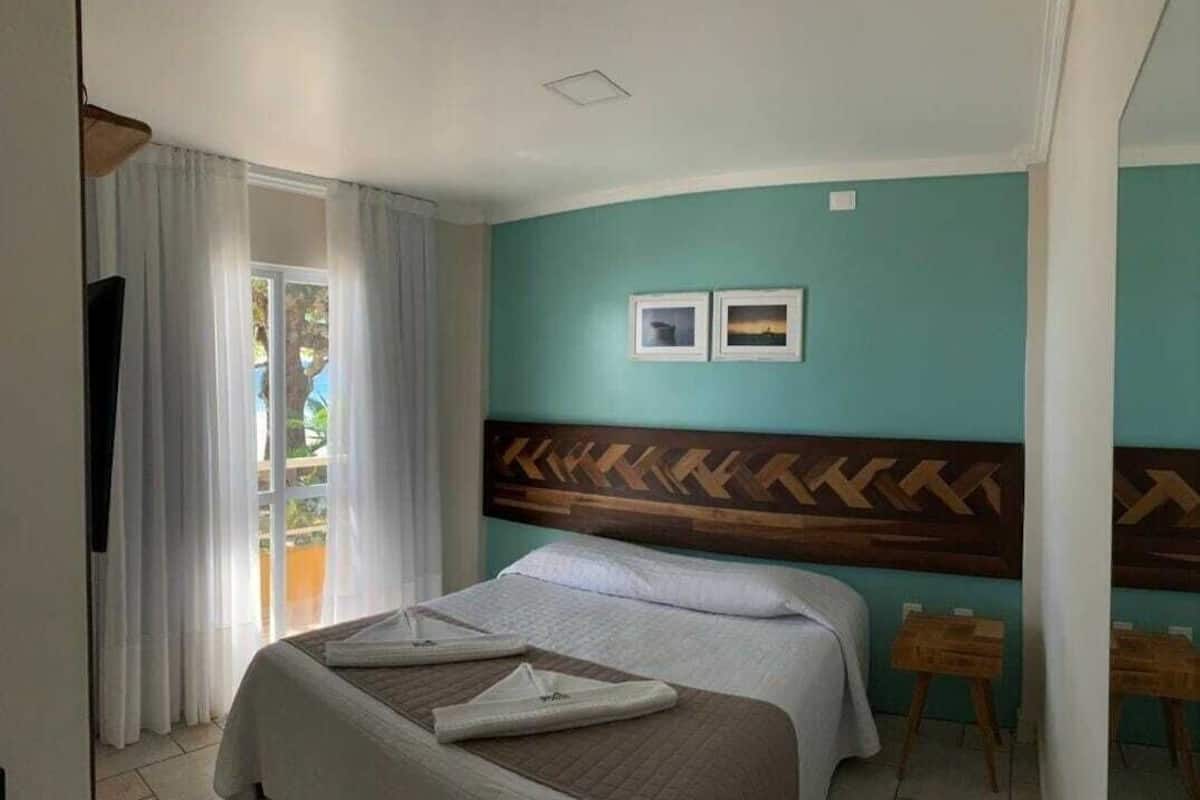 Ein Hotelzimmer mit Bett, Fernseher, einem Fenster mit Vorhängen und zwei gerahmten Bildern an der Wand.