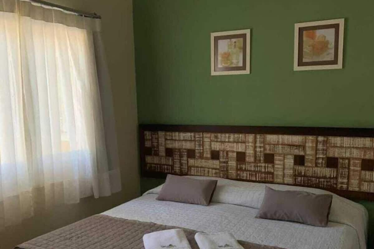 Ein Hotelzimmer mit einem großen Bett, zwei Kissen, einem Kopfende mit Muster und zwei gerahmten Bildern an der Wand.