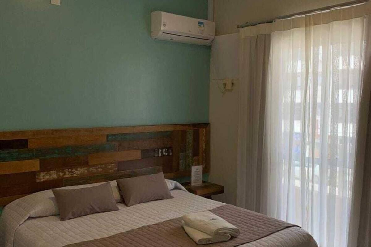 Ein Hotelzimmer mit Bett, Nachttisch, Klimaanlage und einem Fenster mit Vorhängen.