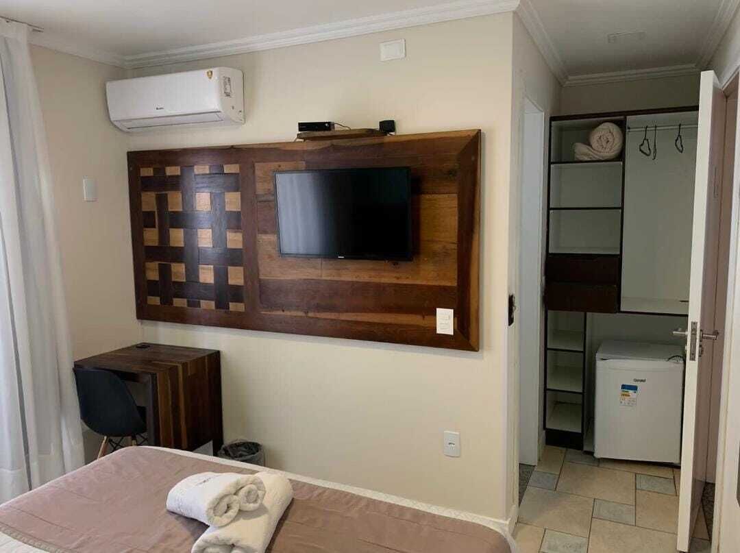 A hotel room with a bed, a desk, a TV mounted on a wooden panel, a mini-fridge, and a walk-in closet.