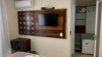 A hotel room with a bed, a desk, a TV mounted on a wooden panel, a mini-fridge, and a walk-in closet.