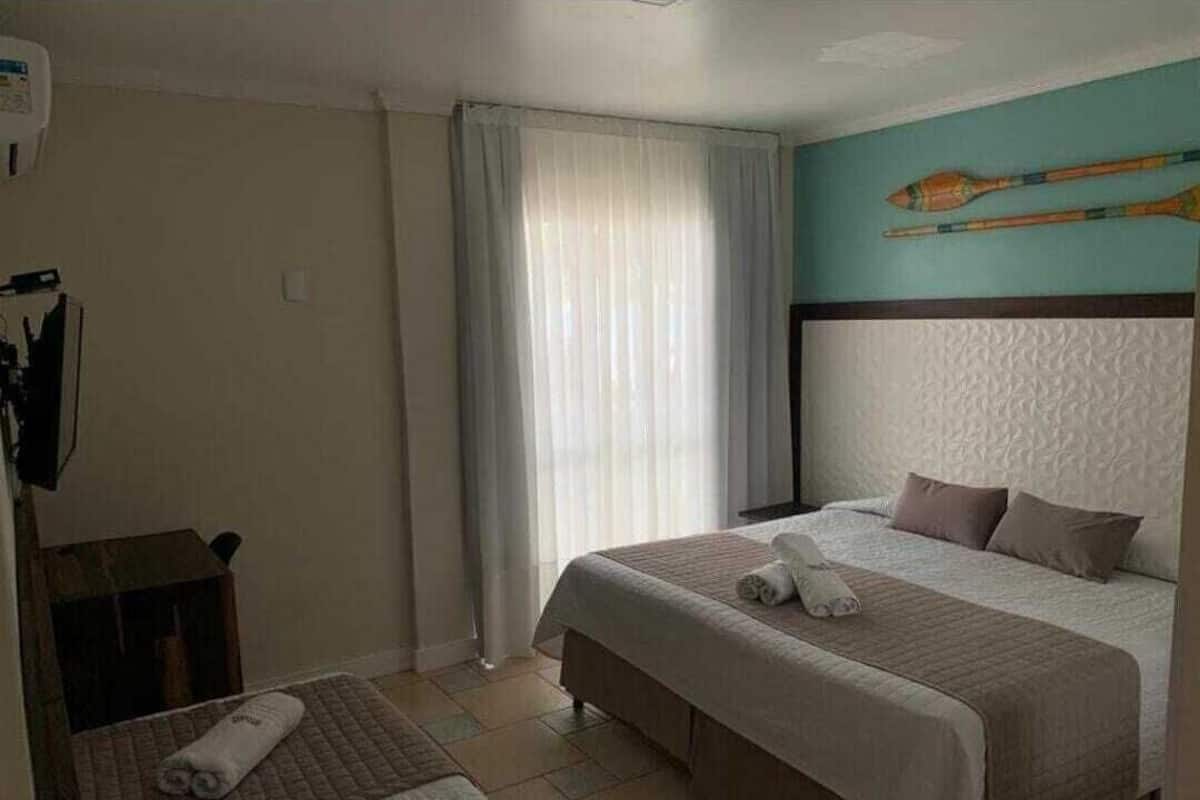 Ein Hotelzimmer mit Bett, Schreibtisch, Stuhl, einem Fenster mit Vorhängen und einem an der Wand befestigten Gegenstand.