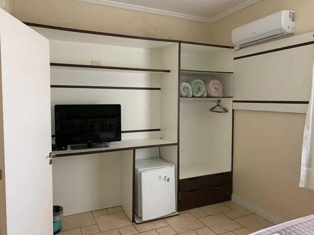 A compact room with a built-in TV, a small fridge, and a wardrobe with shelves and hanging space.
