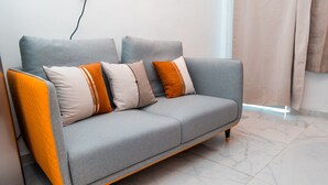 Een grijze bank met oranje en beige kussens in een kamer met een marmeren vloer.