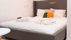 Een netjes opgemaakt bed met witte lakens, een gevouwen handdoek en een smartphone aan de linkerkant.