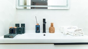 A bathroom sink with various toiletries including a pineapple-shaped soap, a bottle of perfume, and neatly folded towels.