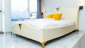 A modern hotel room with a large bed, a view of mountains through the window, and a balcony.