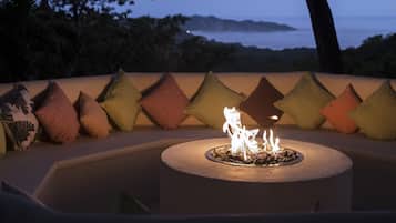 A circular outdoor seating area with a fire feature, surrounded by a row of patterned cushions.