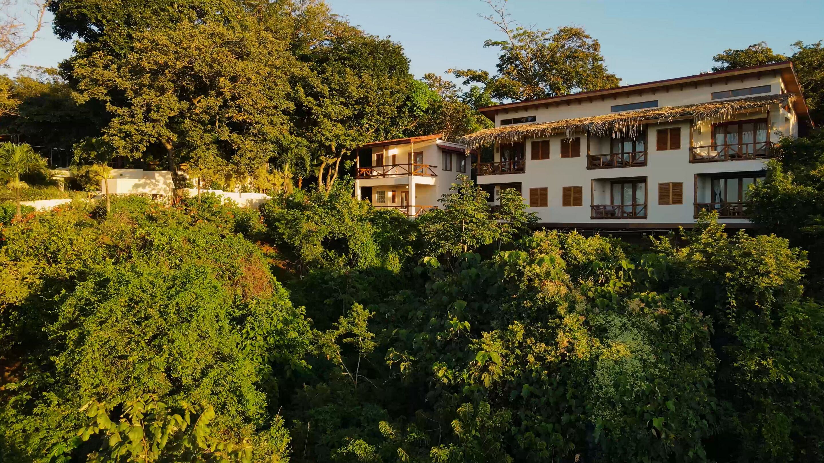 A multi-story building with a thatched roof and balconies, surrounded by dense greenery.