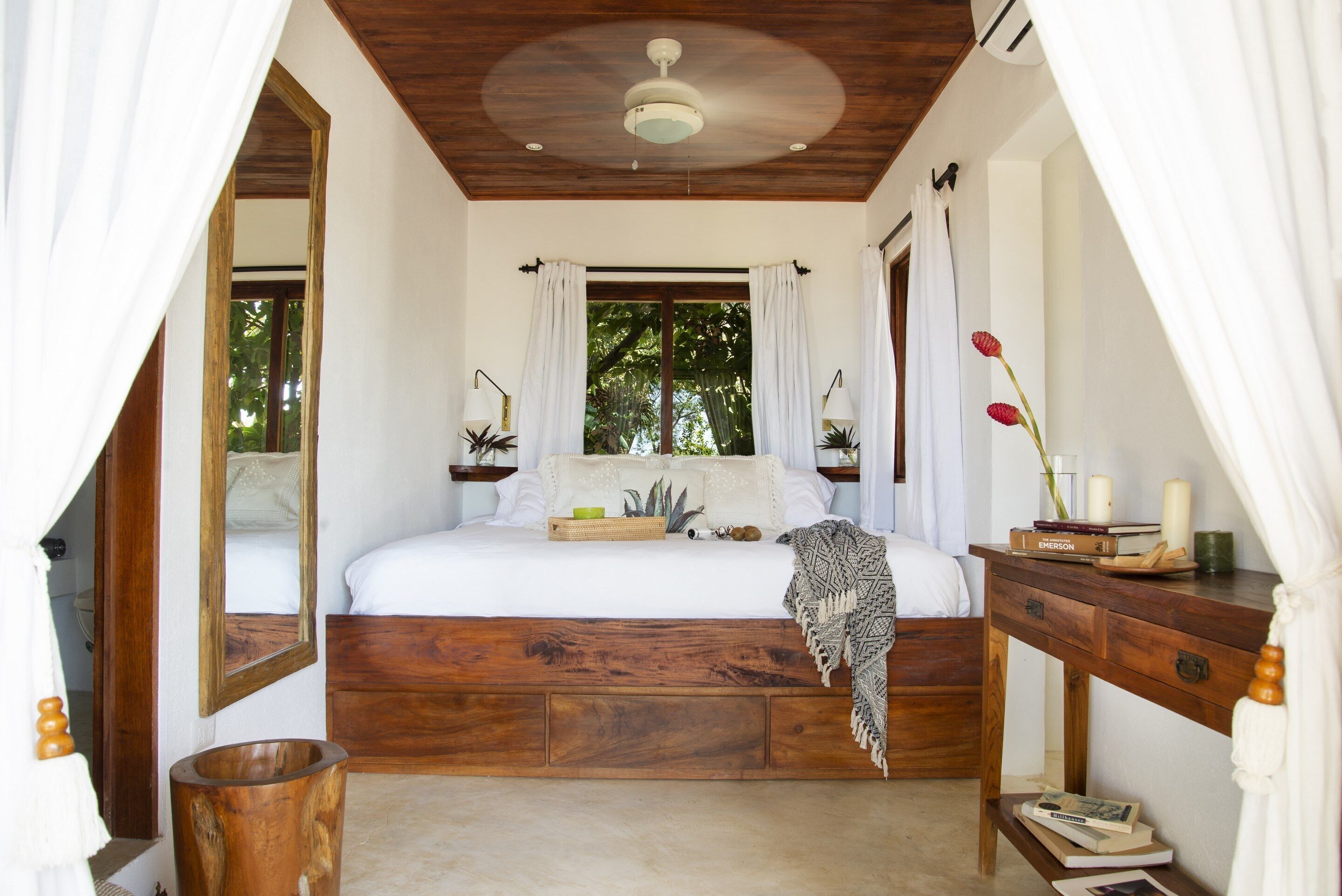 Un dormitorio con una cama de madera, una mesita de noche, un espejo y una ventana con cortinas.