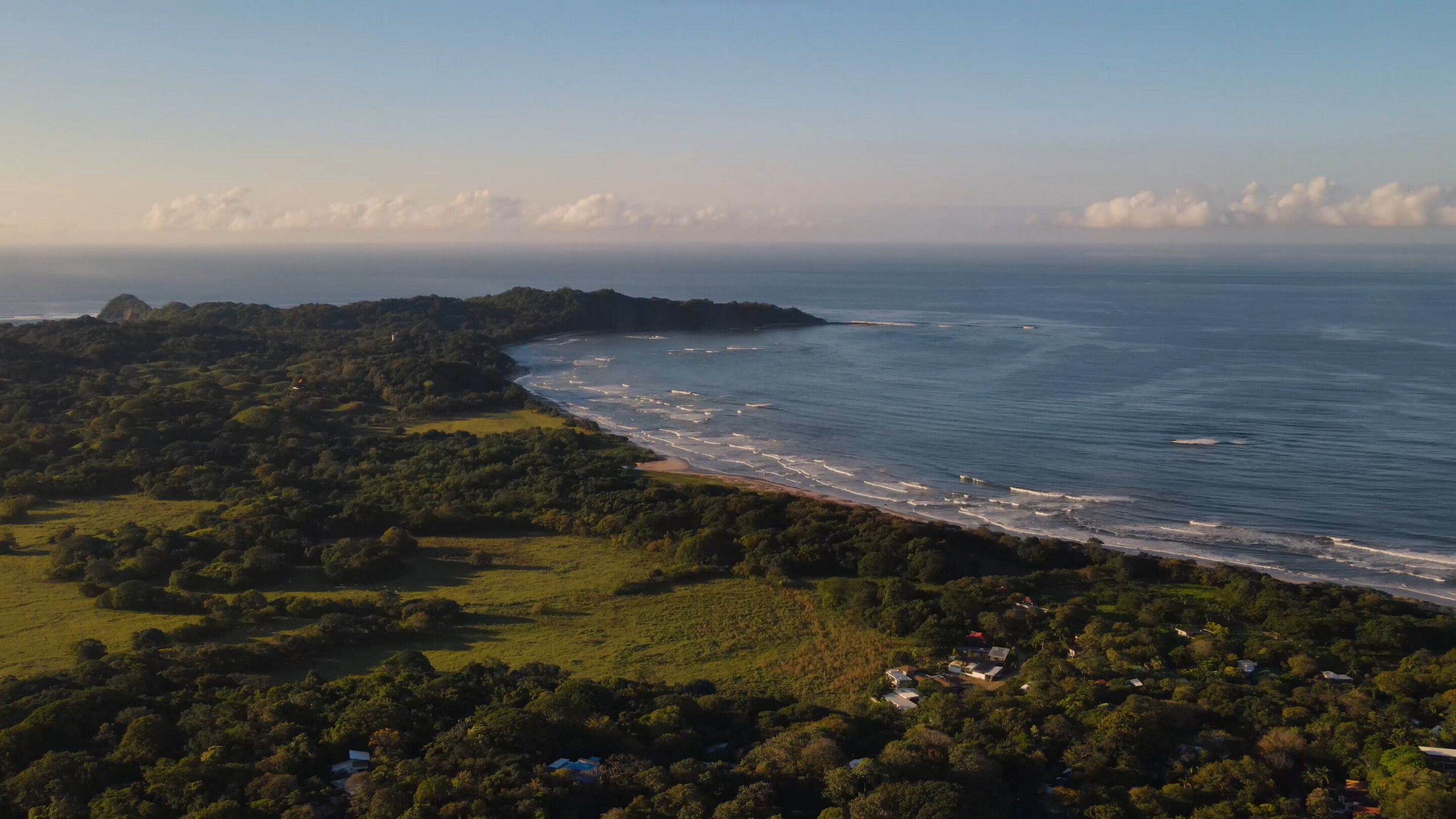 Vue aérienne d’une zone côtière avec une plage, de la végétation et quelques bâtiments dispersés.