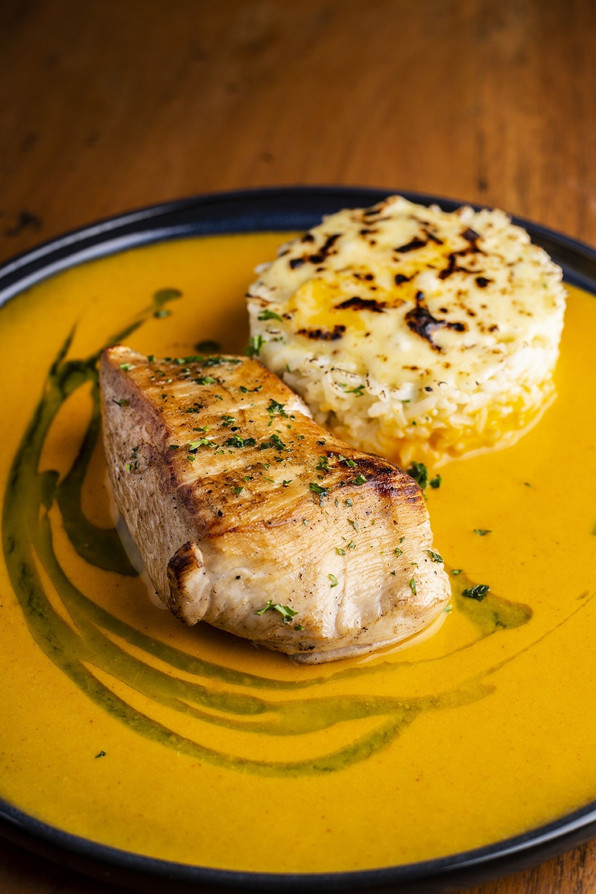 Ein Teller mit gegrilltem Fisch und Kartoffelpüree vor gelblicher Hintergrund.