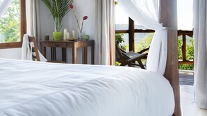 A bedroom with a canopy bed, a wooden table with candles, a potted plant, and a view of the outdoors.