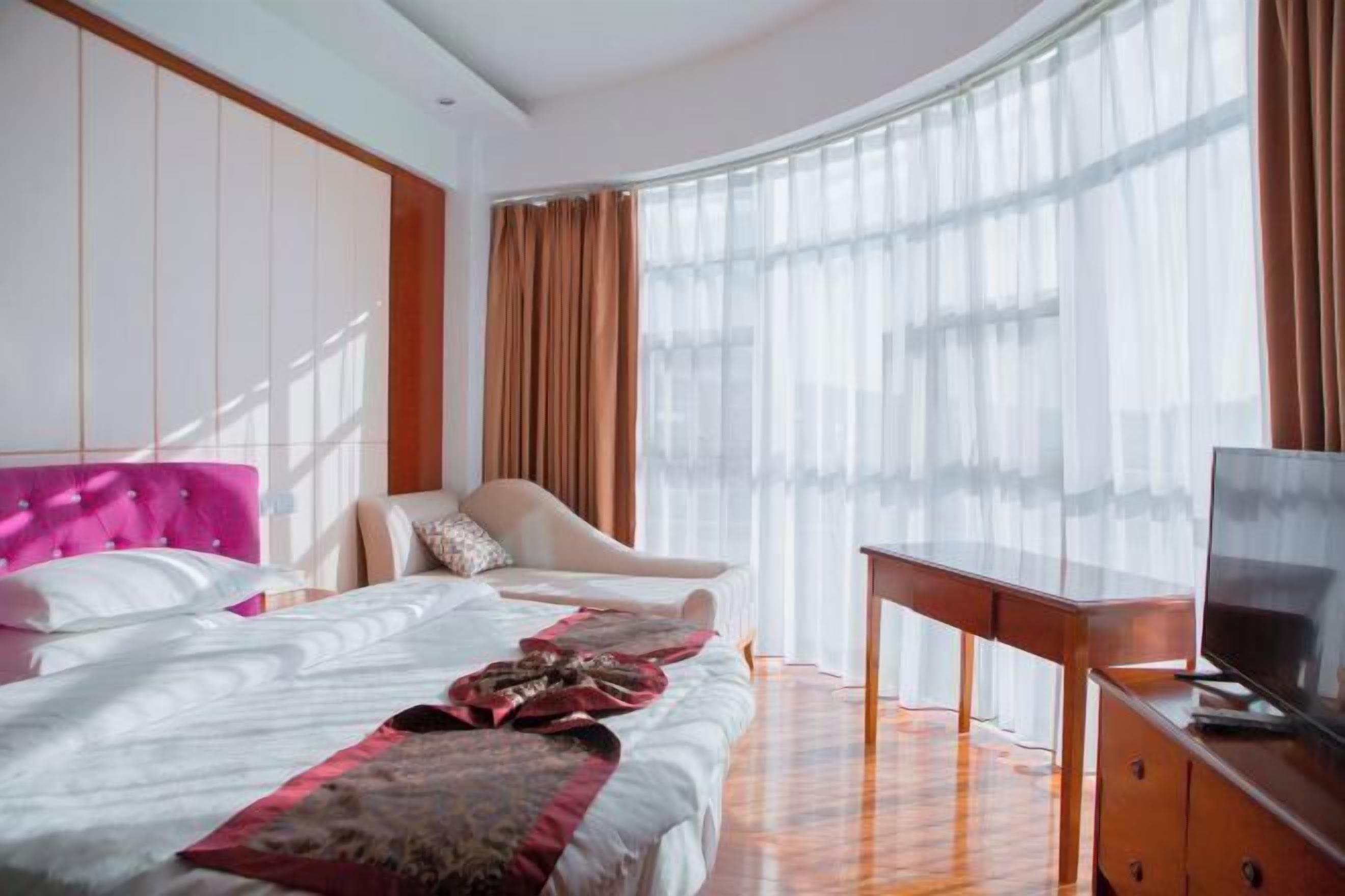 Una habitación de hotel con cama, una silla, televisión y un ventanal con cortinas.