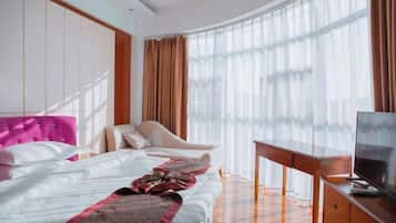 Una habitación de hotel con cama, una silla, televisión y un ventanal con cortinas.