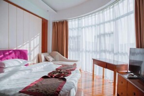 Una habitación de hotel con cama, una silla, televisión y un ventanal con cortinas.
