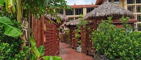 Un sendero de madera que conduce a un edificio con construcciones de techo de paja y abundante vegetación.