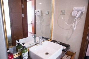 Un baño con un lavamanos blanco, dos secadores de pelo fijados en la pared y un espejo sobre el lavamanos.