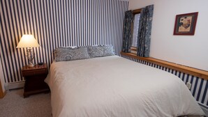 A neatly made bed with a white comforter and patterned pillows, a bedside lamp, and a striped wall with a framed picture. - Ski-in/Ski-out | FREE ACCESS Spring House Pool (Ludlow)