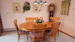 A dining room with a wooden table and chairs, a chandelier, a wall clock, and framed artwork. - Ski-in/Ski-out | FREE ACCESS Spring House Pool (Ludlow)