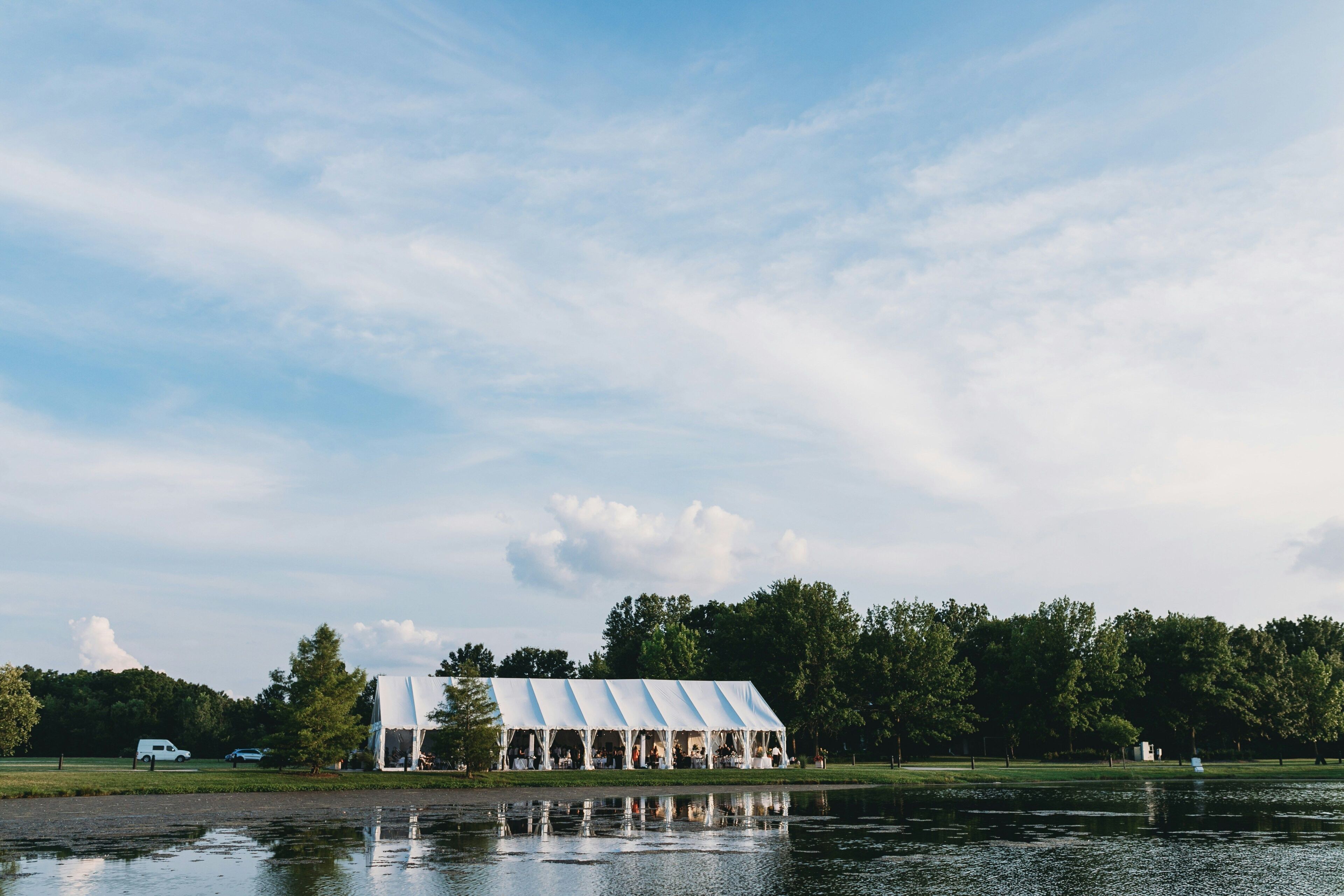 A lakeside pavilion with a reflective water surface, surrounded by trees and a clear sky.
