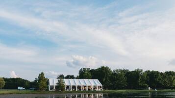A lakeside pavilion with a reflective water surface, surrounded by trees and a clear sky.