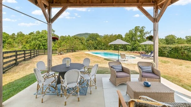Un patio exterior techado con piscina, muebles de mimbre y vistas del paisaje circundante.