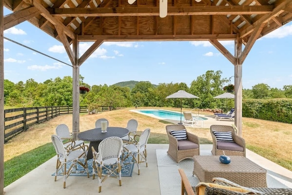 Un patio exterior techado con piscina, muebles de mimbre y vistas del paisaje circundante.