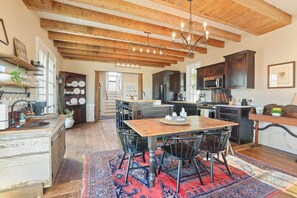 A kitchen with wooden beams, a dining table with chairs, and a red patterned rug.