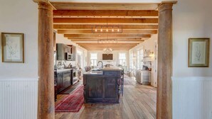 Una cocina amplia con vigas de madera, una isla central y vistas a habitaciones contiguas.