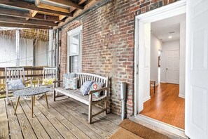 A wooden deck with a bench and table, a brick wall, and an open doorway leading to an interior space.