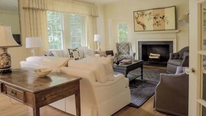 A living room with a fireplace, a sofa, a coffee table, and a chair. - Hoos` Homestead | Historic UVA area home (Charlottesville)