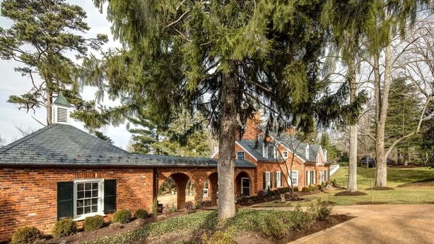 A brick house with a sloped roof, a small attached structure with a green roof, and a large tree in the foreground. - Hoos` Homestead | Historic UVA area home (Charlottesville)
