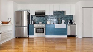 Una cucina moderna con mobili bianchi, un frigorifero in acciaio inossidabile, un forno, un microonde e uno schienale blu.
