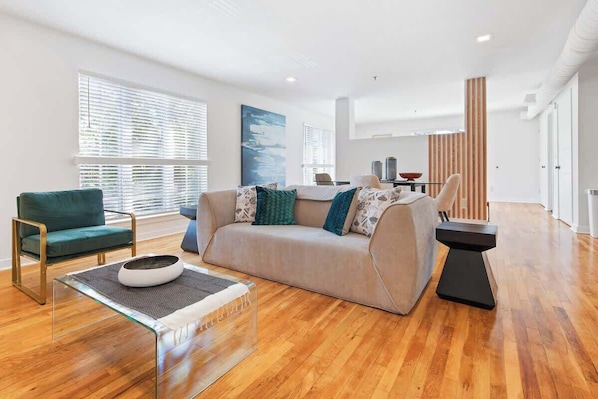 A modern living room with a sofa, a chair, a coffee table, and a dining area in the background.