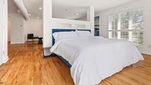Una camera da letto con un letto grande, pavimento in legno, pareti bianche e una finestra con persiane.