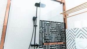 Een moderne badkamer met een douchecabine van glas, een handdoekrek met zwart-wit patroon, en een wand met een witte, gevlekte textuur.