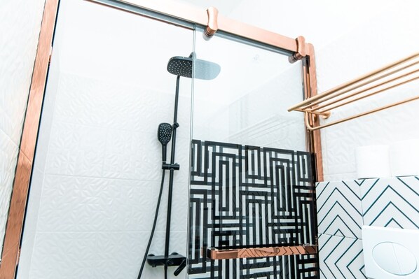 Un baño moderno con cabina de ducha de vidrio, un perchero con toallas de diseño blanco y negro y una pared blanca con textura.